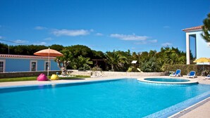 A swimming pool with lounge chairs and umbrellas, surrounded by greenery and a building with a blue facade. - Hotel Neptuno (Peniche)