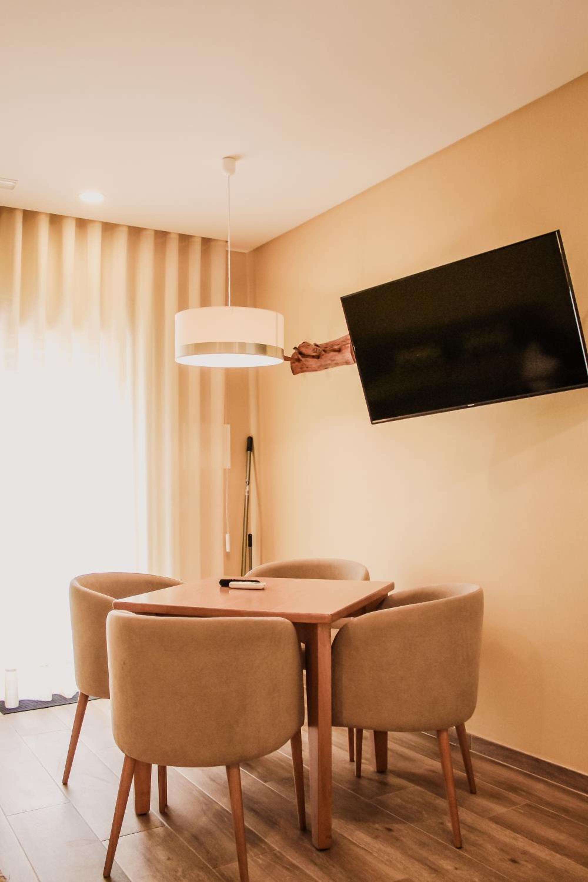 A modern dining area with a wooden table, four chairs, a mounted flat-screen TV, and a pendant light.