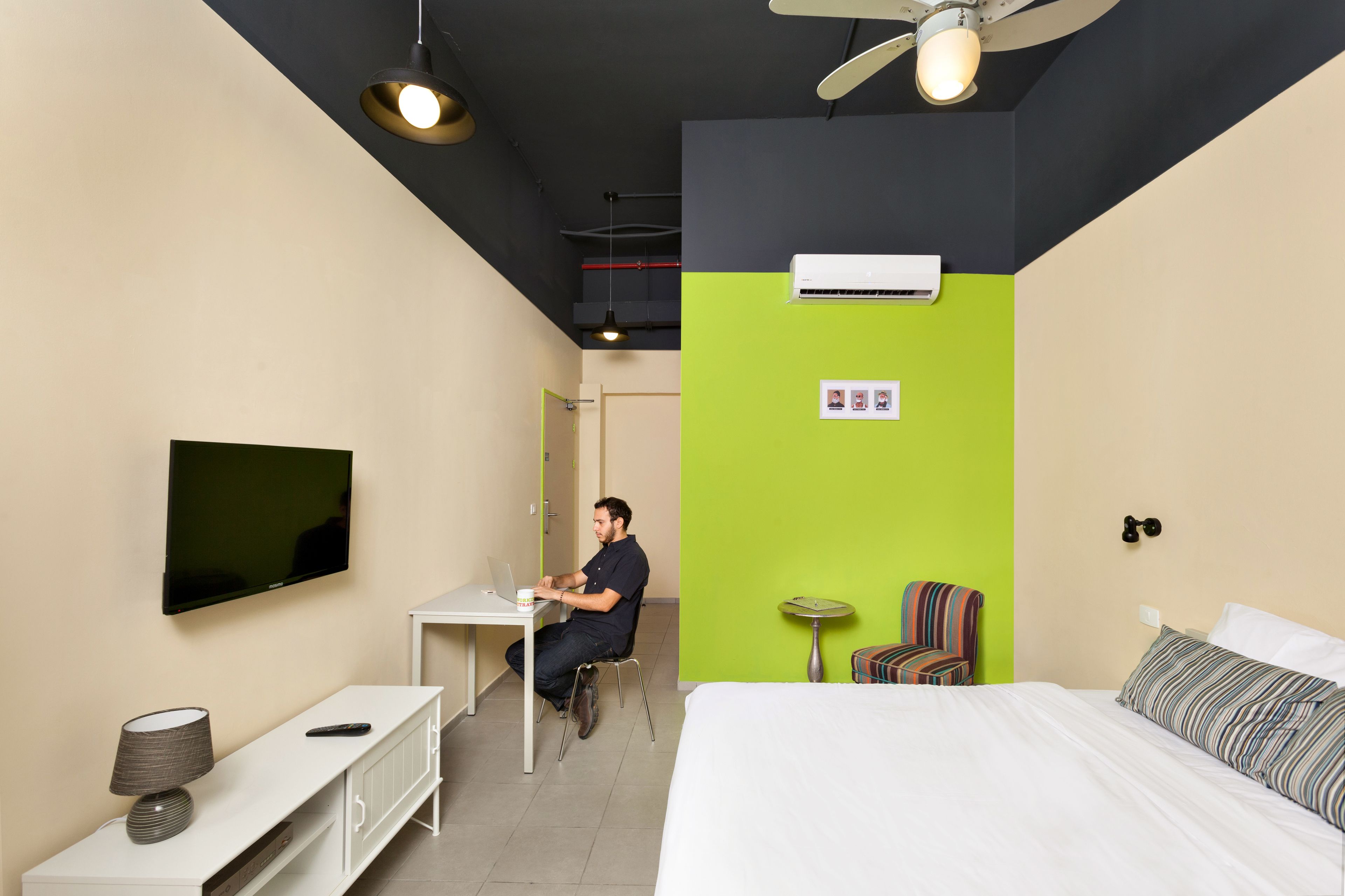 Een hotelkamer met een bed, een bureau, een stoel, een televisie en een airconditioner.