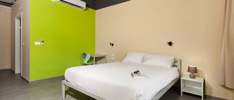Een hotelkamer met een bed, een nachtkastje met een lamp, een groene wand en een airconditioning.
