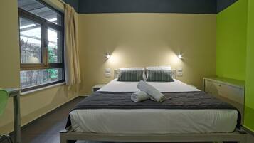 A hotel room with a bed, bedside lamps, a window with curtains, and a green accent wall.