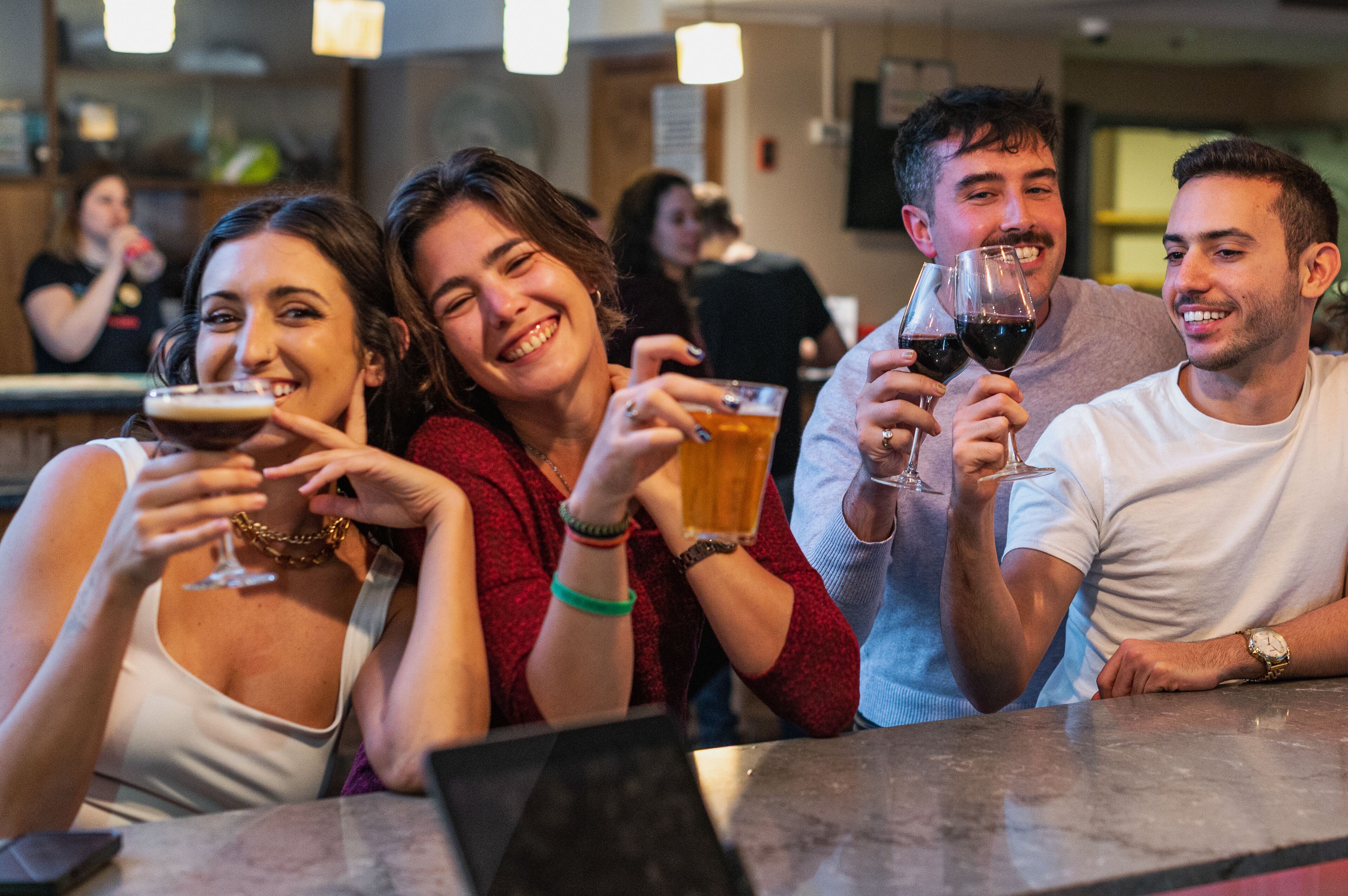 A group of people sitting at a bar, holding glasses of beer and wine.
