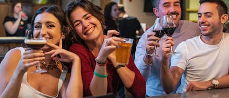 Un grupo de personas sentadas en un bar, sosteniendo vasos de cerveza y vino.