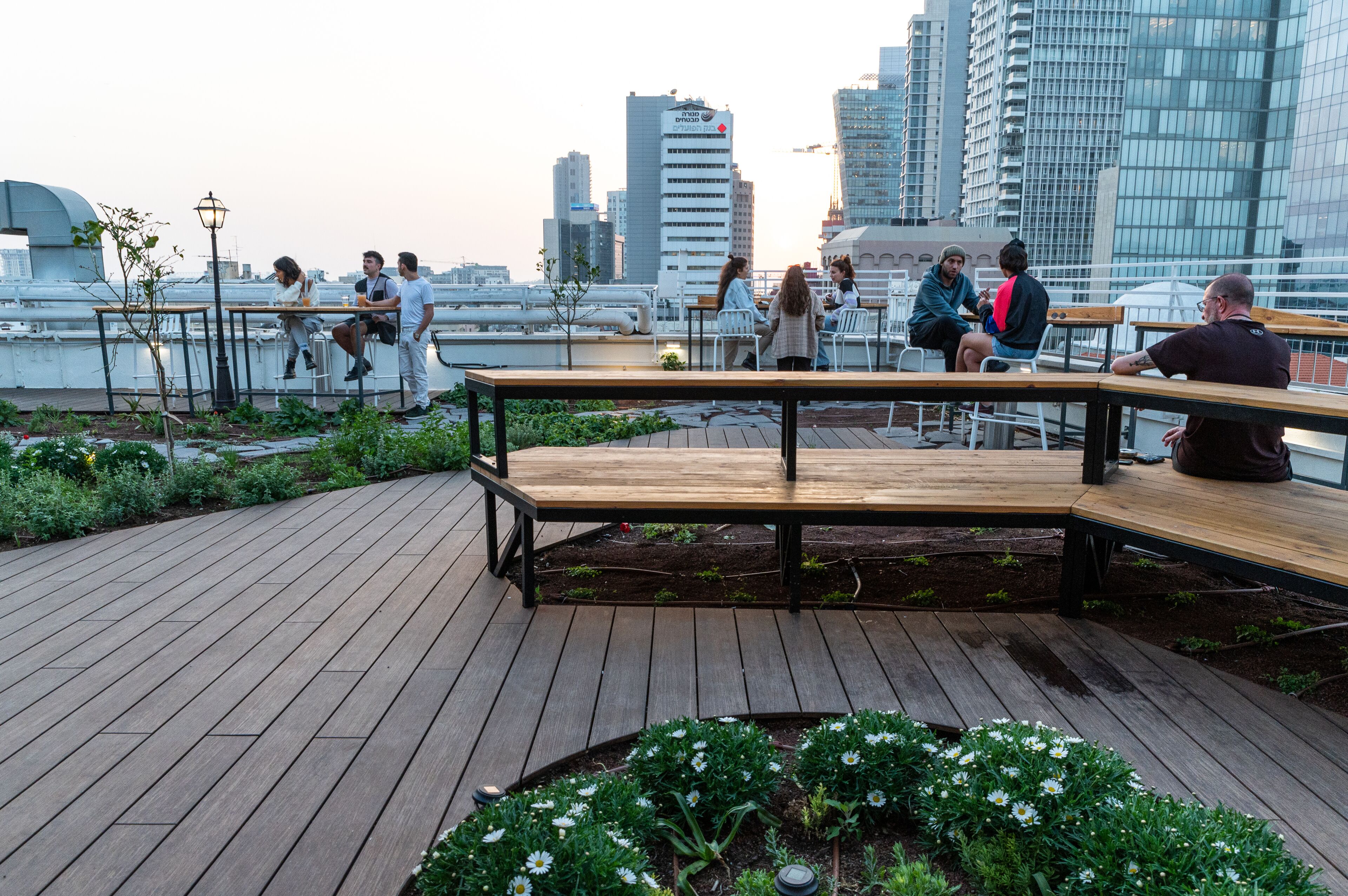 A wooden deck with benches and tables, surrounded by greenery and flowers.