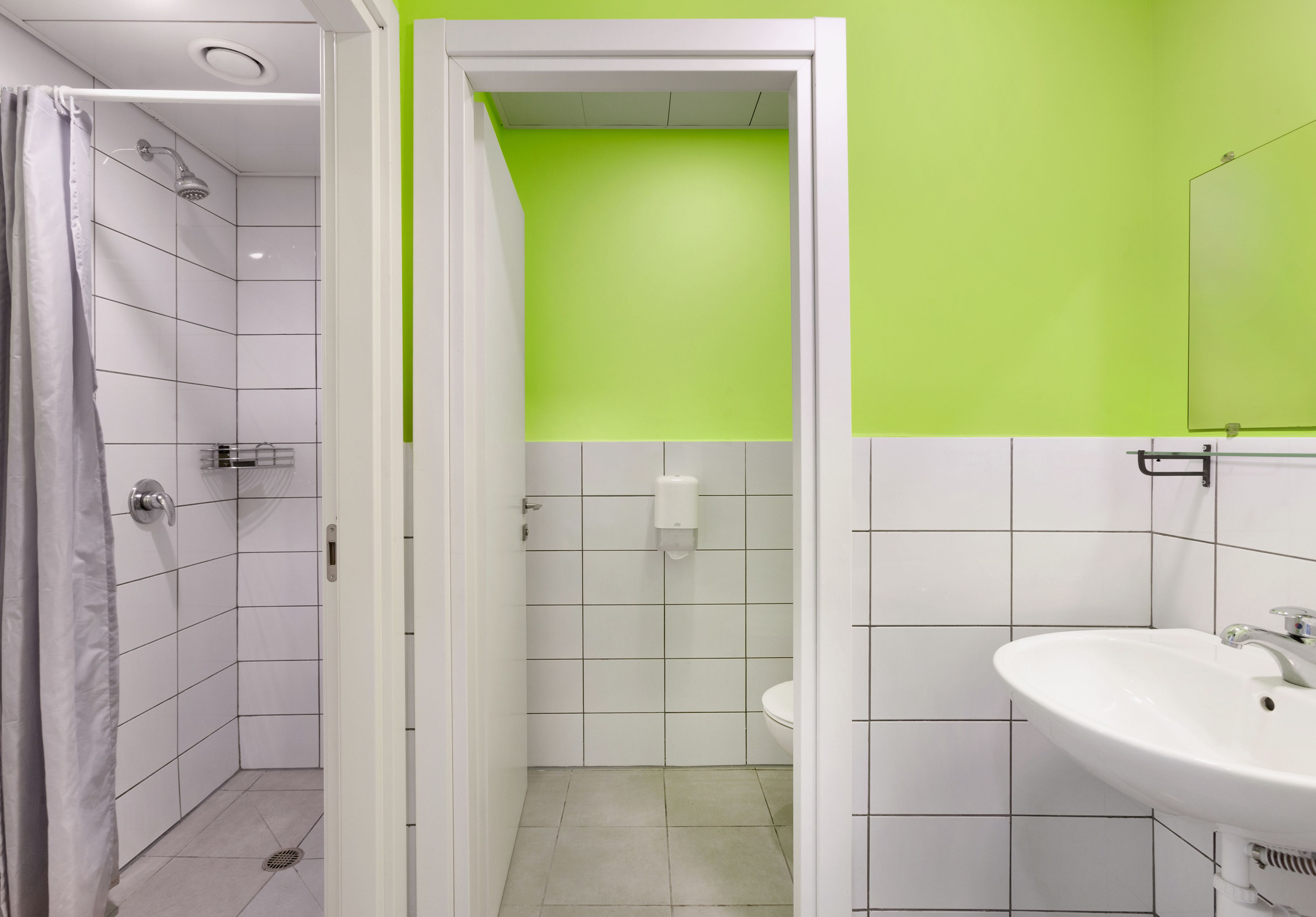 A bathroom with white tiles, a green accent wall, a shower, and a sink.