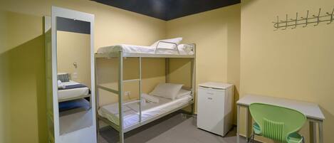 A dormitory room with bunk beds, a desk, a chair, and a small refrigerator.