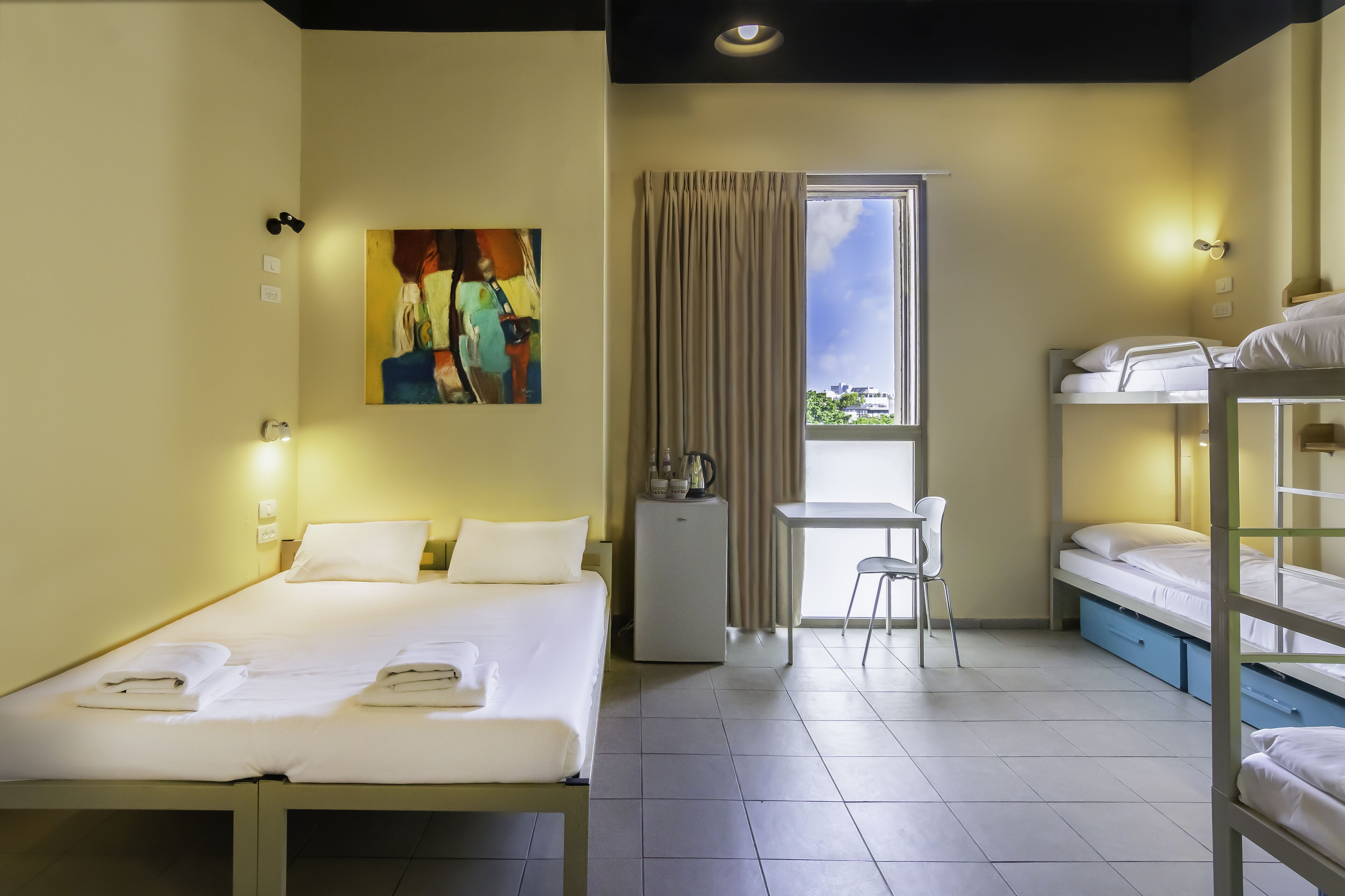 A hotel room with a single bed, a desk, a chair, and a bunk bed.