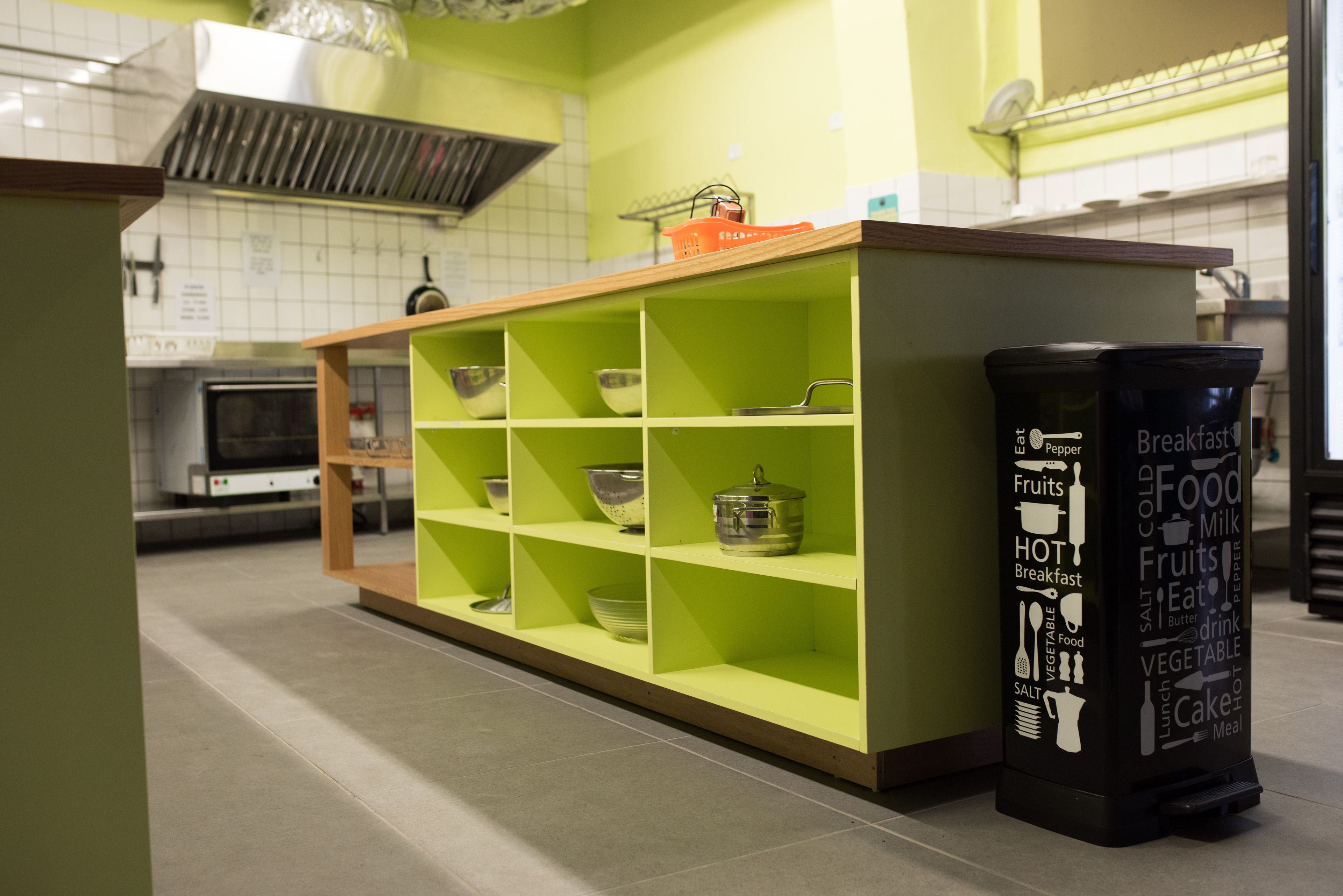 A kitchen area with green shelves, a microwave, and a black refrigerator with food-related stickers.