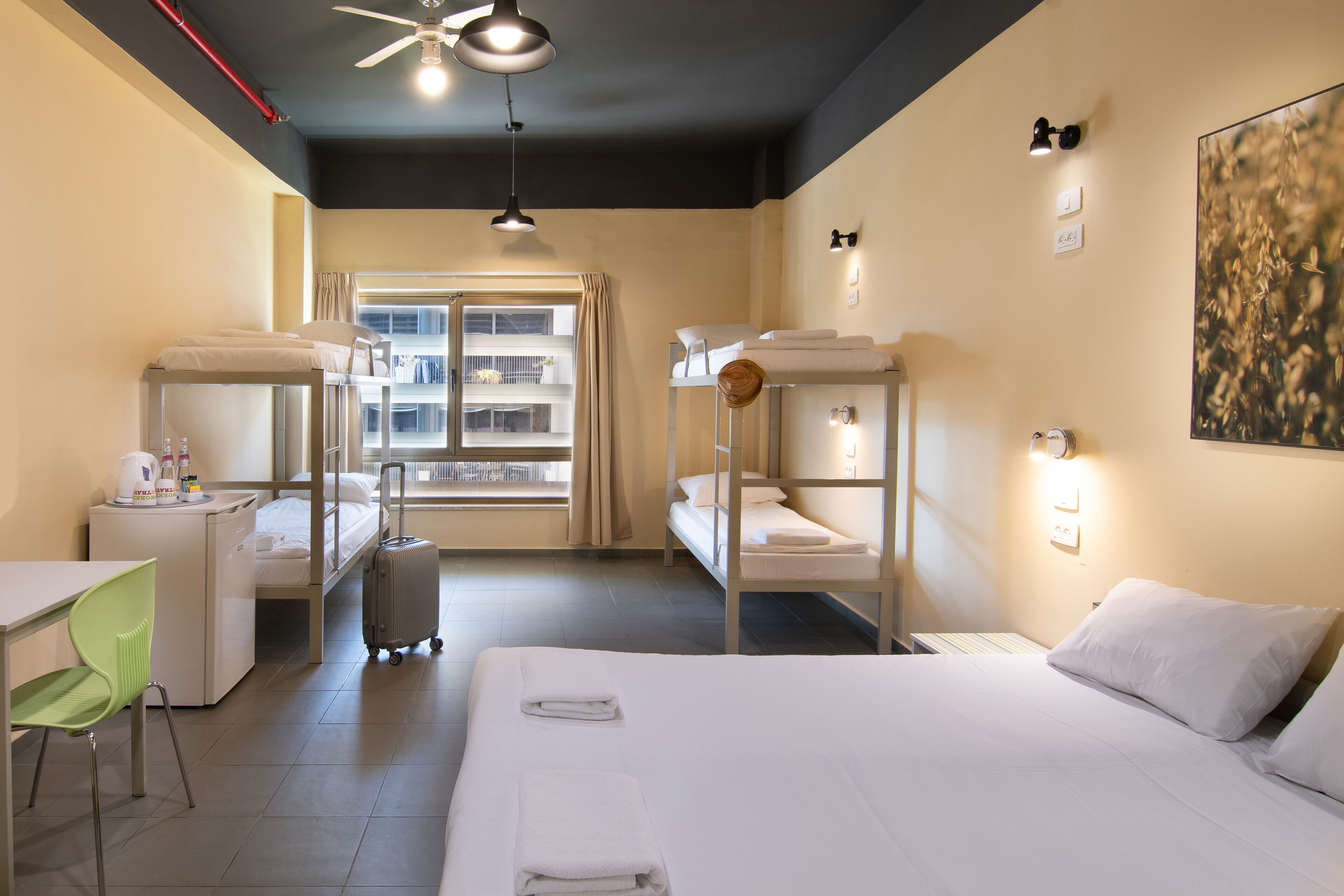 A hotel room with bunk beds, a desk, a chair, a suitcase, and a window with curtains.