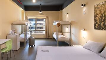 A hotel room with bunk beds, a desk, a chair, a suitcase, and a window with curtains.