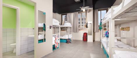 A dormitory room with bunk beds, a bathroom, and a window with curtains.