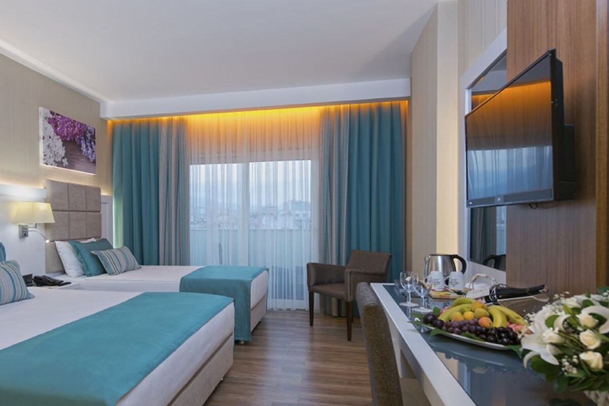 A hotel room with two beds, a desk with a fruit platter, a coffee maker, and a TV.