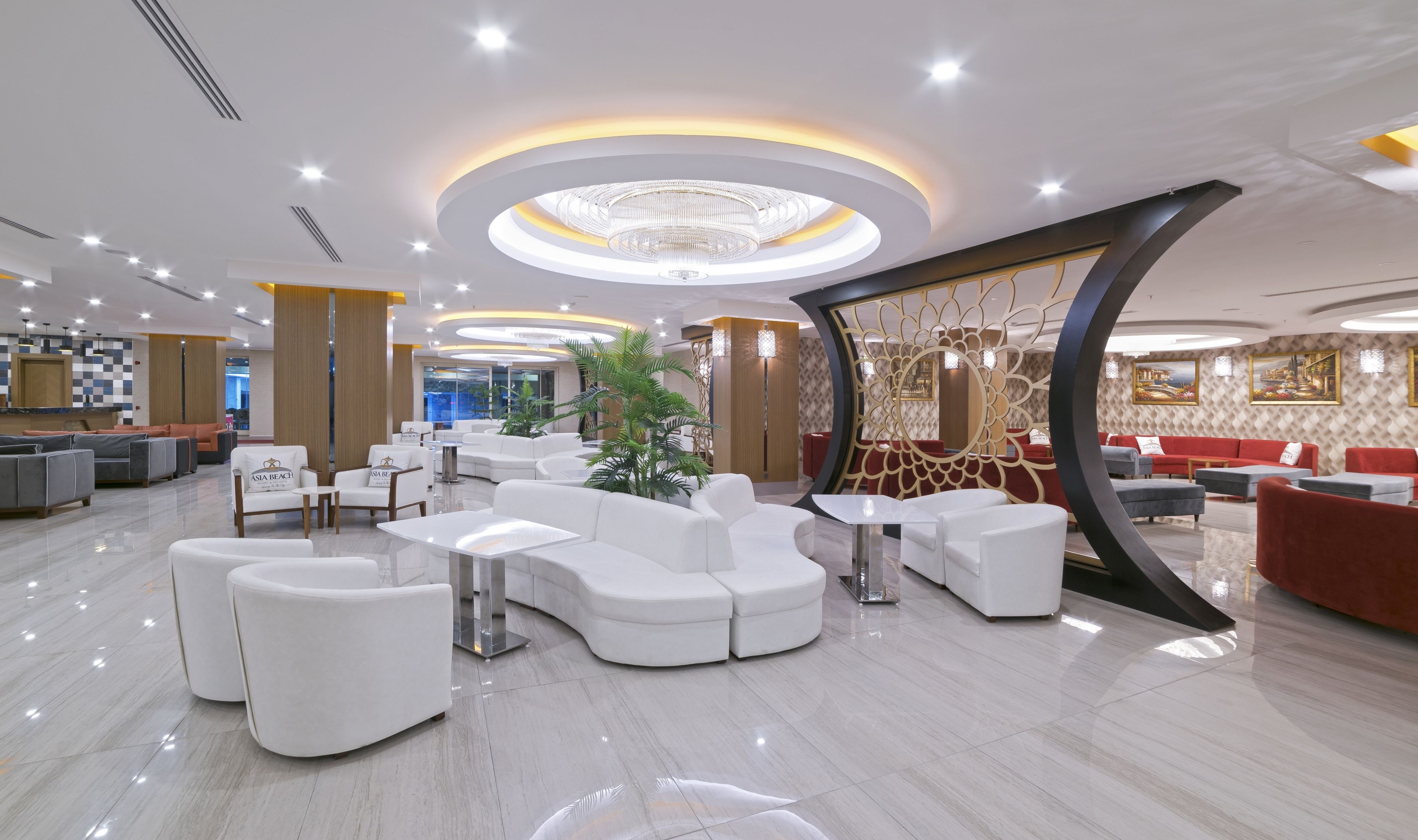 A modern hotel lobby with white sofas, a central plant, and a decorative wall with a circular design.