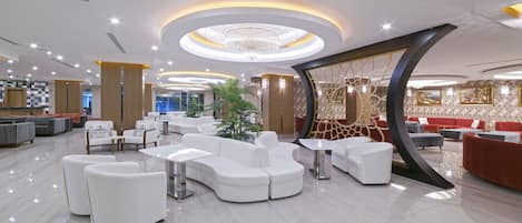 A modern hotel lobby with white sofas, a central plant, and a decorative wall with a circular design.