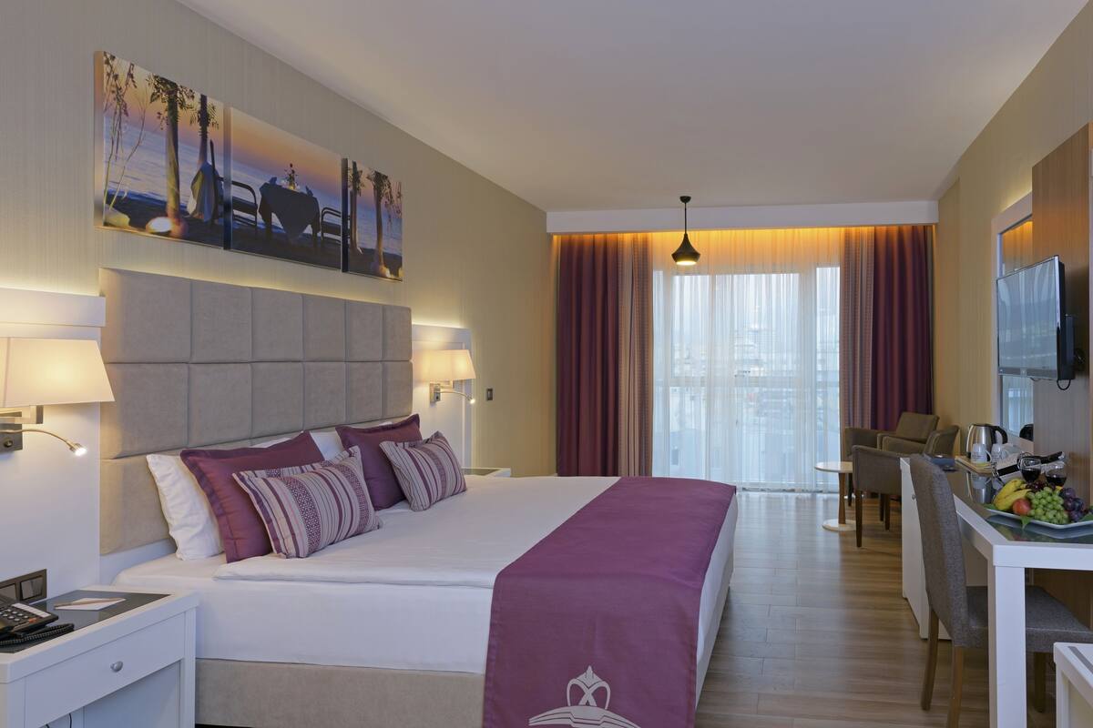 Habitación de hotel con una cama grande, un escritorio con silla, televisor y zona de comedor con mesa para dos.