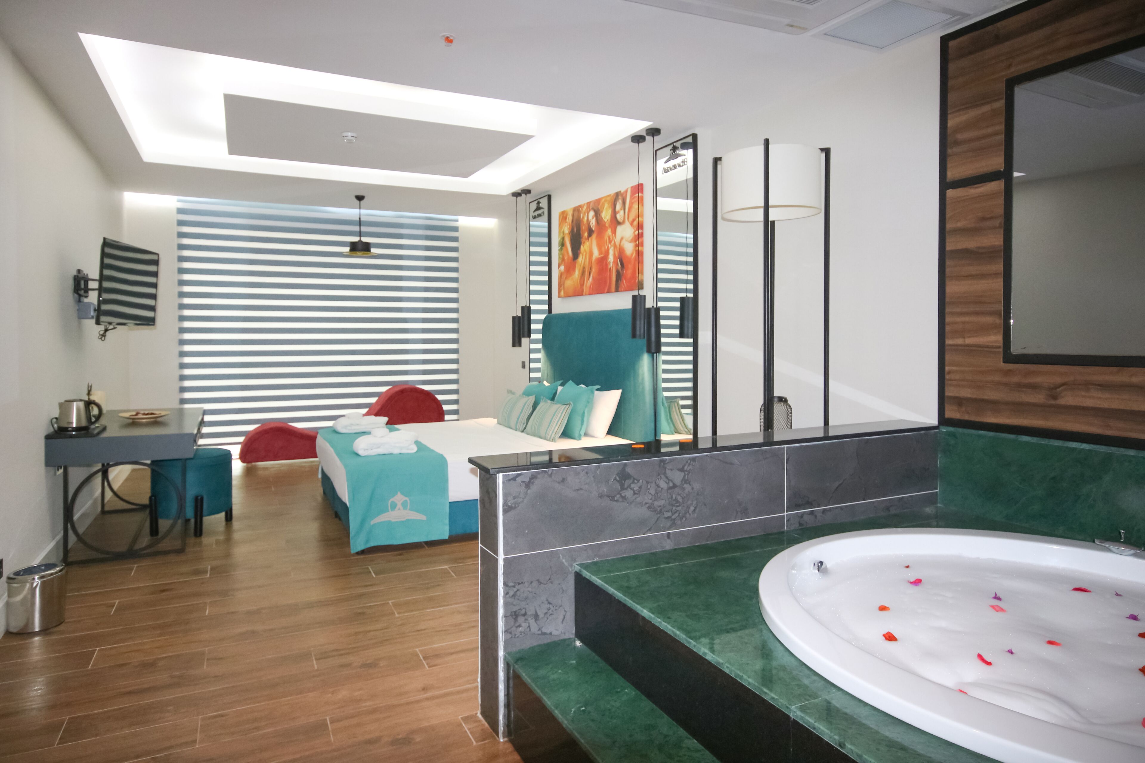A modern bedroom with a bed, a desk, a bathroom with a bathtub, and a large mirror.