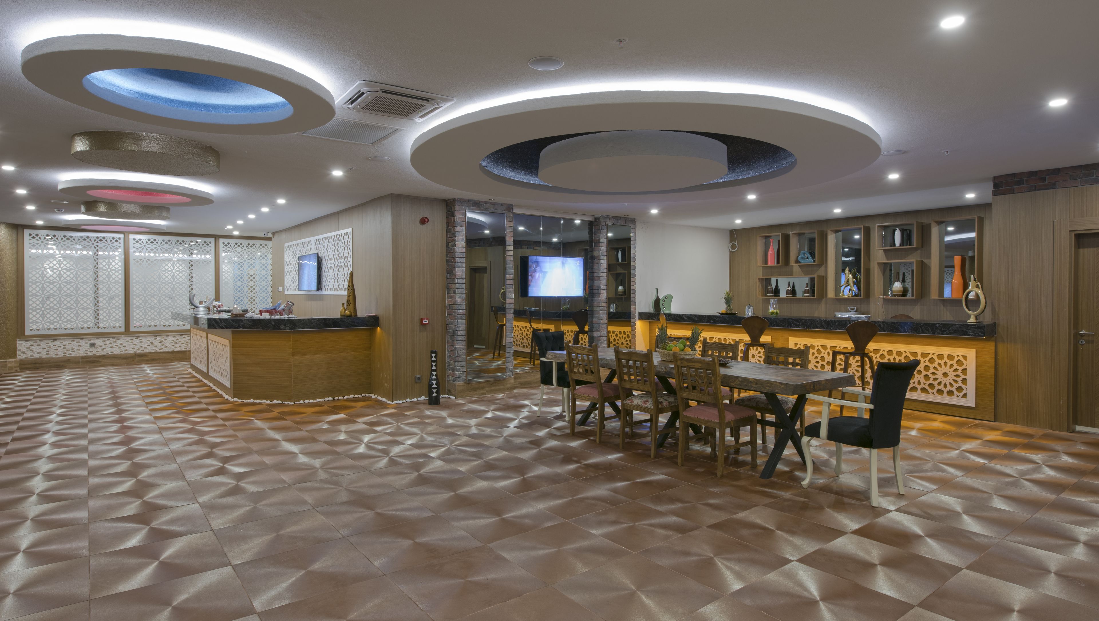 A modern restaurant with a central dining area, a bar, and a TV screen.