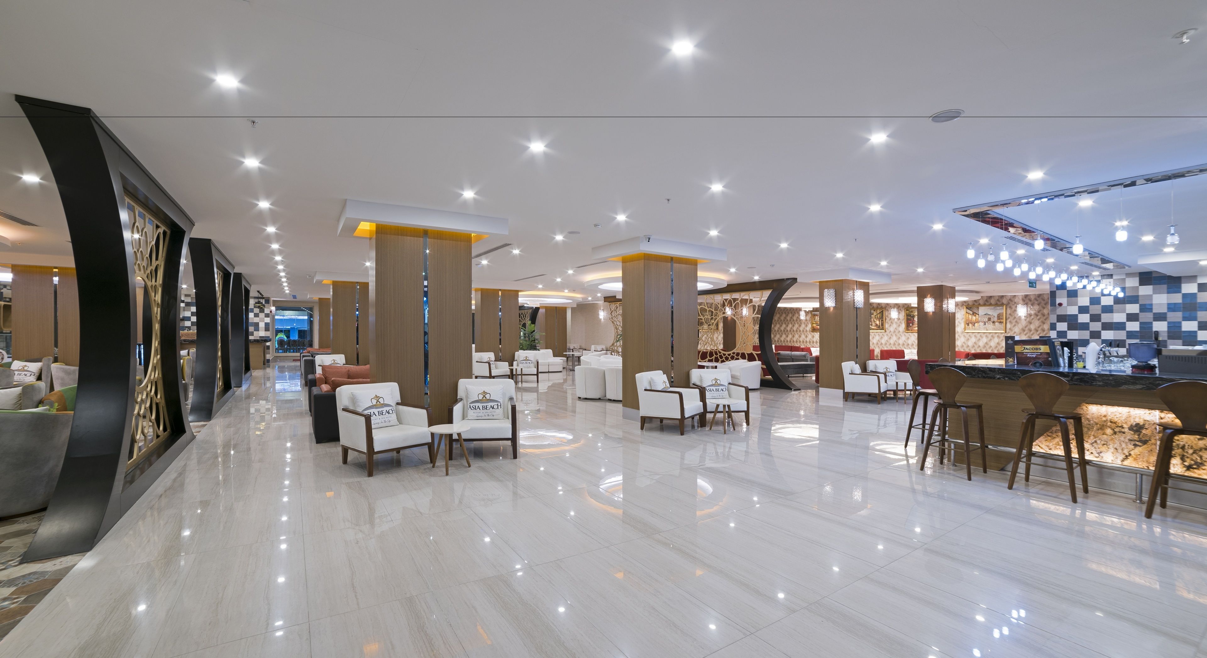 A spacious lobby with a checkered floor pattern, multiple seating areas with white chairs, and a bar counter.