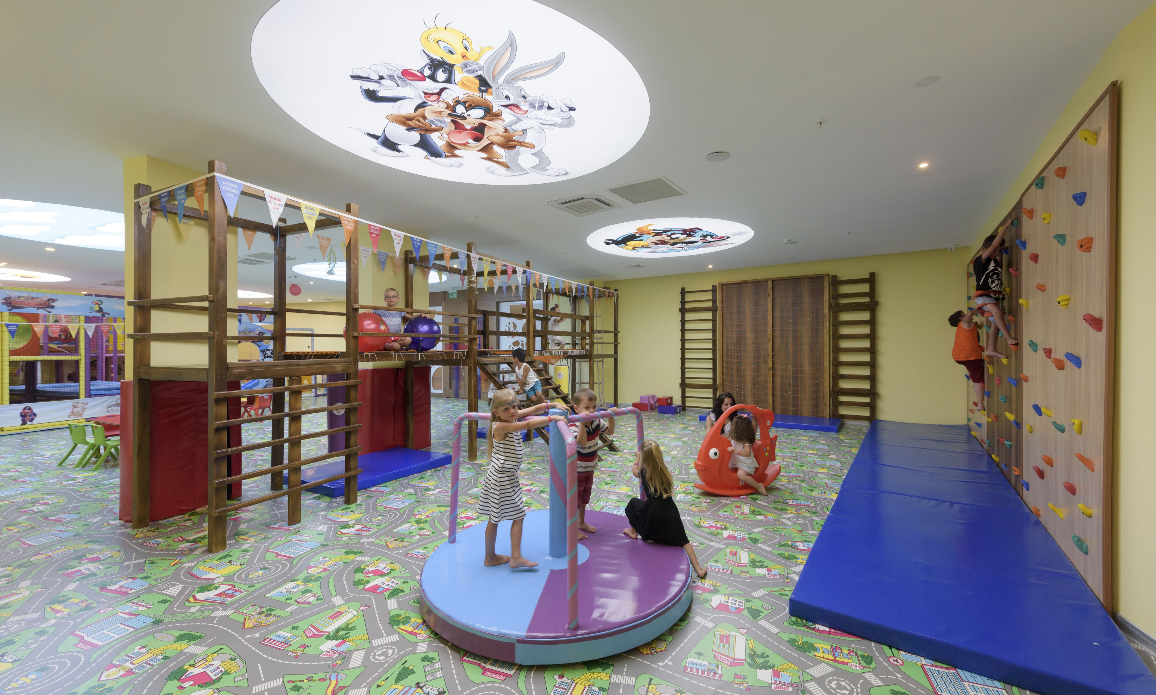 A children's play area with a climbing structure, soft play floor, and colorful wall decorations.