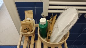Um banquinho de madeira com um cesto contendo sacolas de papel, uma garrafa verde e um objeto embrulhado.