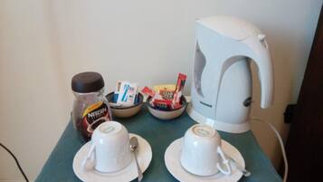 Angolo cottura con macchina del caffè, due tazze, un barattolo di Nescafe e una ciotola di bustine di zucchero.