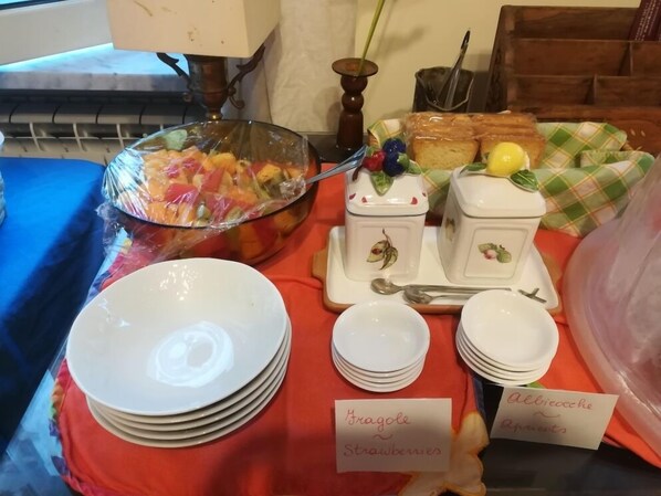 A buffet table with labeled dishes of strawberries and apricots, surrounded by white plates and bowls. - B&B Cupole e Campanili (Naples)