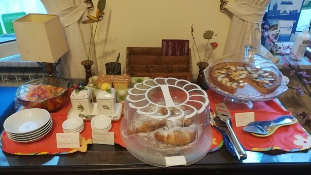 Uma mesa de buffet com diversos alimentos, incluindo um bolo grande, doces e uma saladeira de frutas.