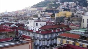 Uma área urbana densamente povoada com diversos estilos e cores de edifícios, incluindo telhados brancos, amarelos e vermelhos.