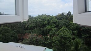A view through a window with a white frame, overlooking a dense green forest and a white building in the distance. - Gia Thanh Guest House (Phu Quoc)
