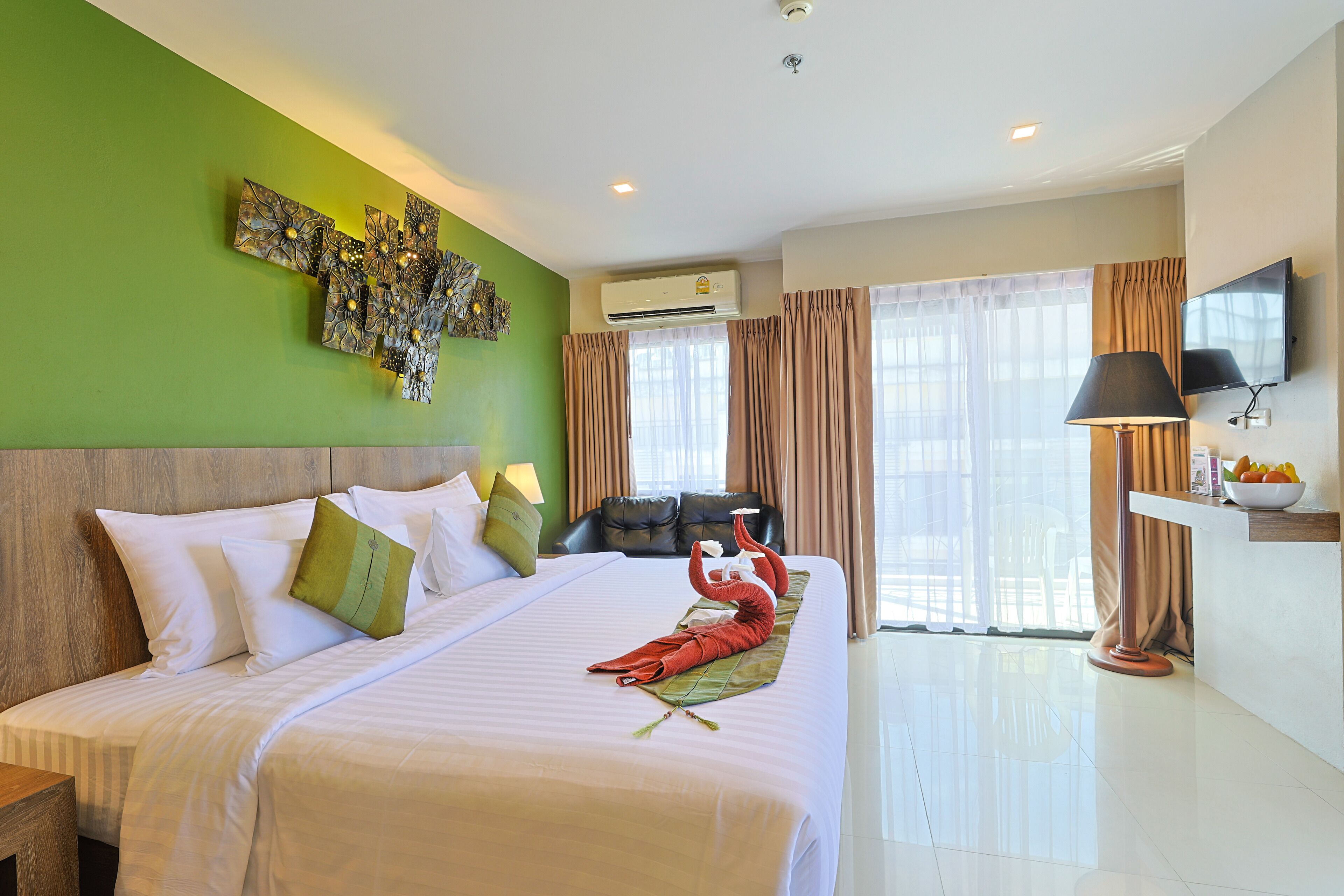 A hotel room with a large bed, a flat-screen TV, a desk with a lamp, and a window with curtains.