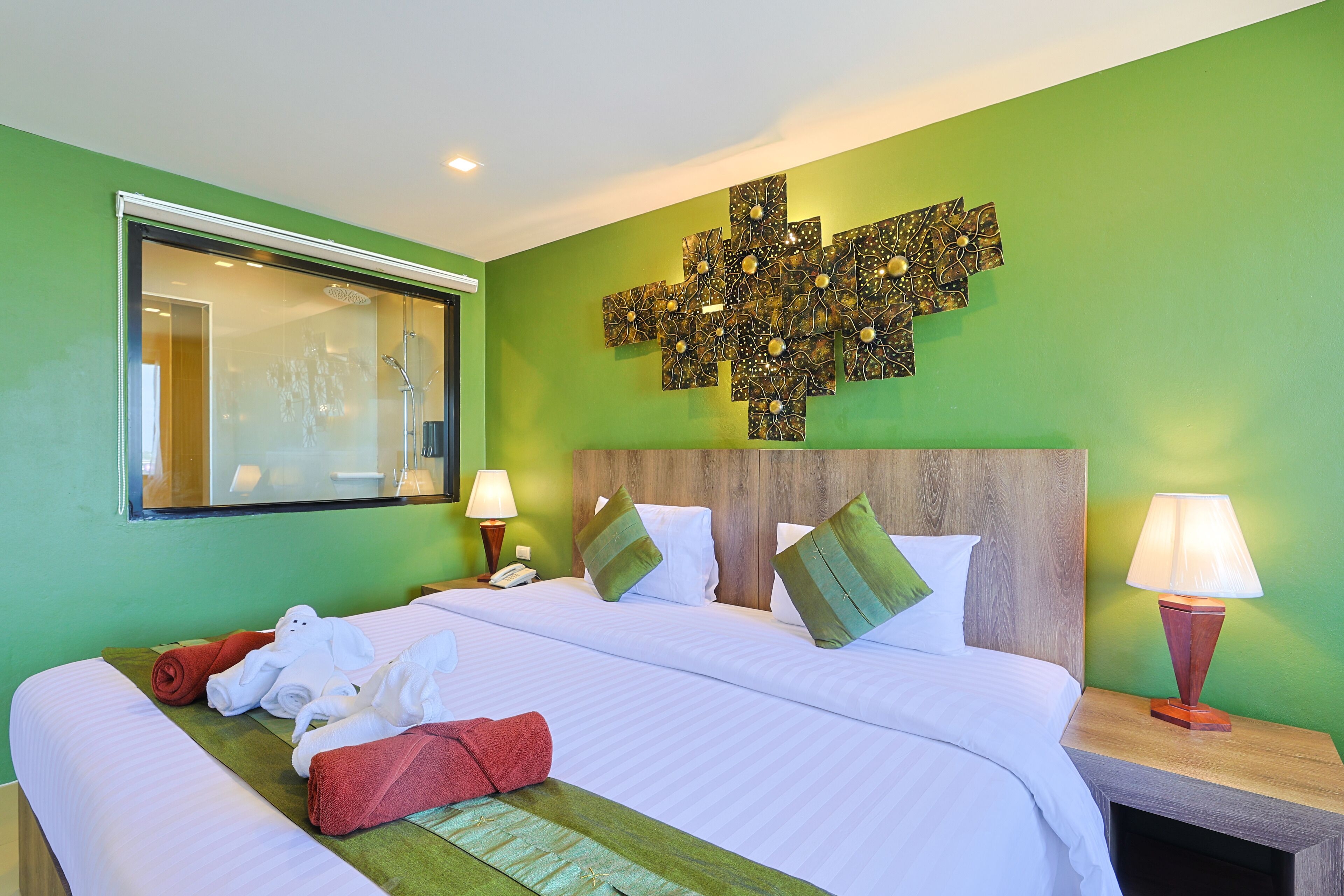 A hotel room with a large bed, green walls, a wooden headboard, and a decorative wall piece above the bed.