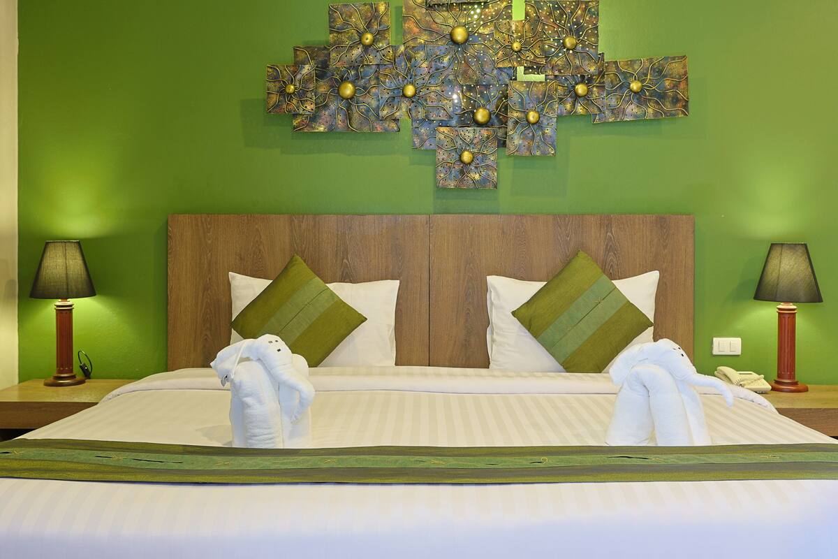 Quarto de hotel com uma cama grande, paredes verdes e um objeto decorativo sobre a cama.