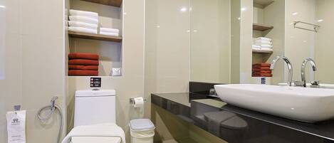 A modern bathroom with a white toilet, a glass shower enclosure, a large mirror, and a black countertop with a white sink.