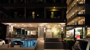 A hotel entrance with a pool, outdoor seating, and a car parked nearby. - The Gig Hotel (Patong)