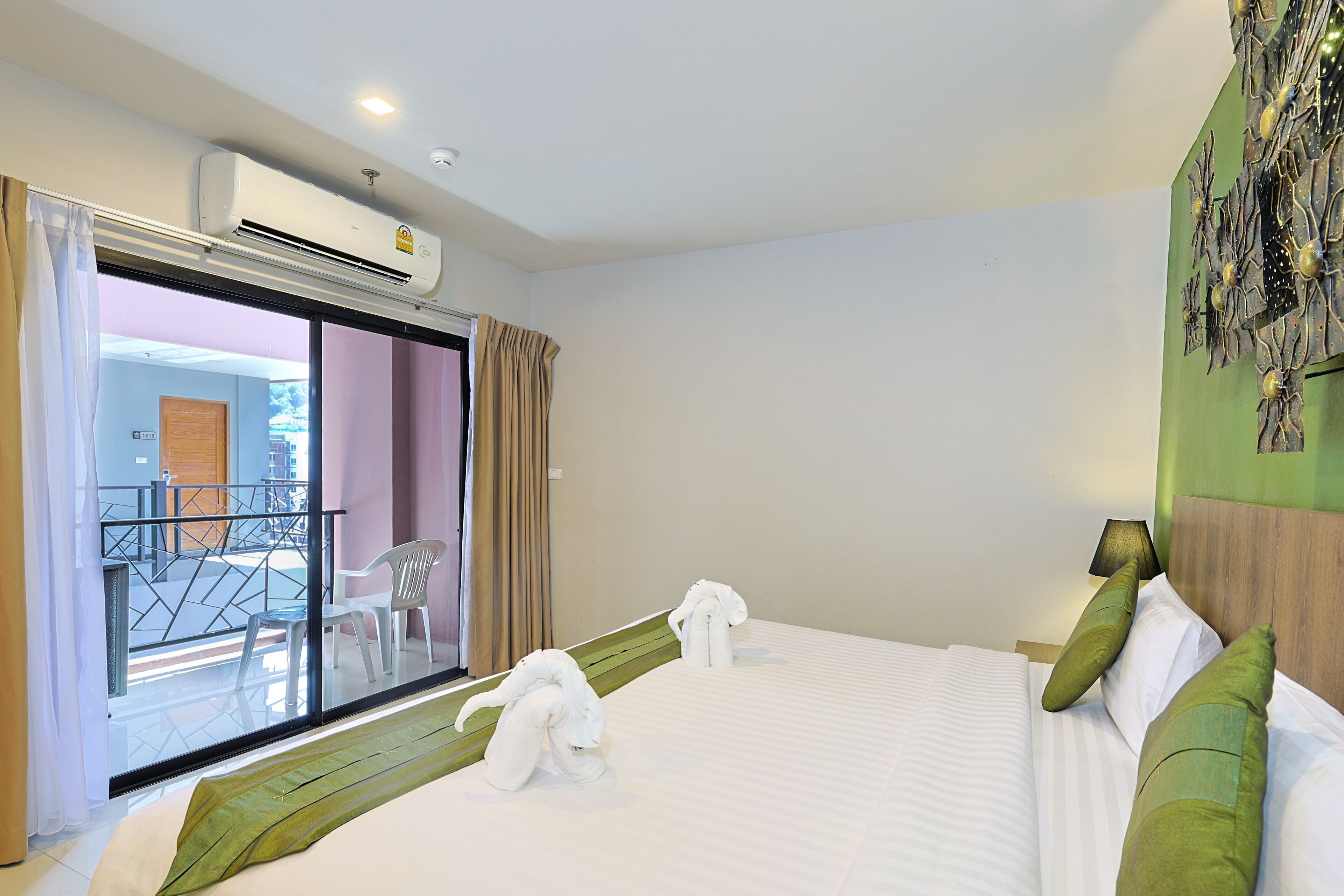 A hotel room with a bed, a window with curtains, a wall-mounted air conditioner, and a view of the outside balcony.