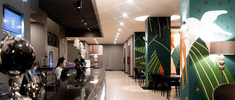 Een moderne hotellobby met een receptiebalie, een zithoek en decoratieve wandkunst.