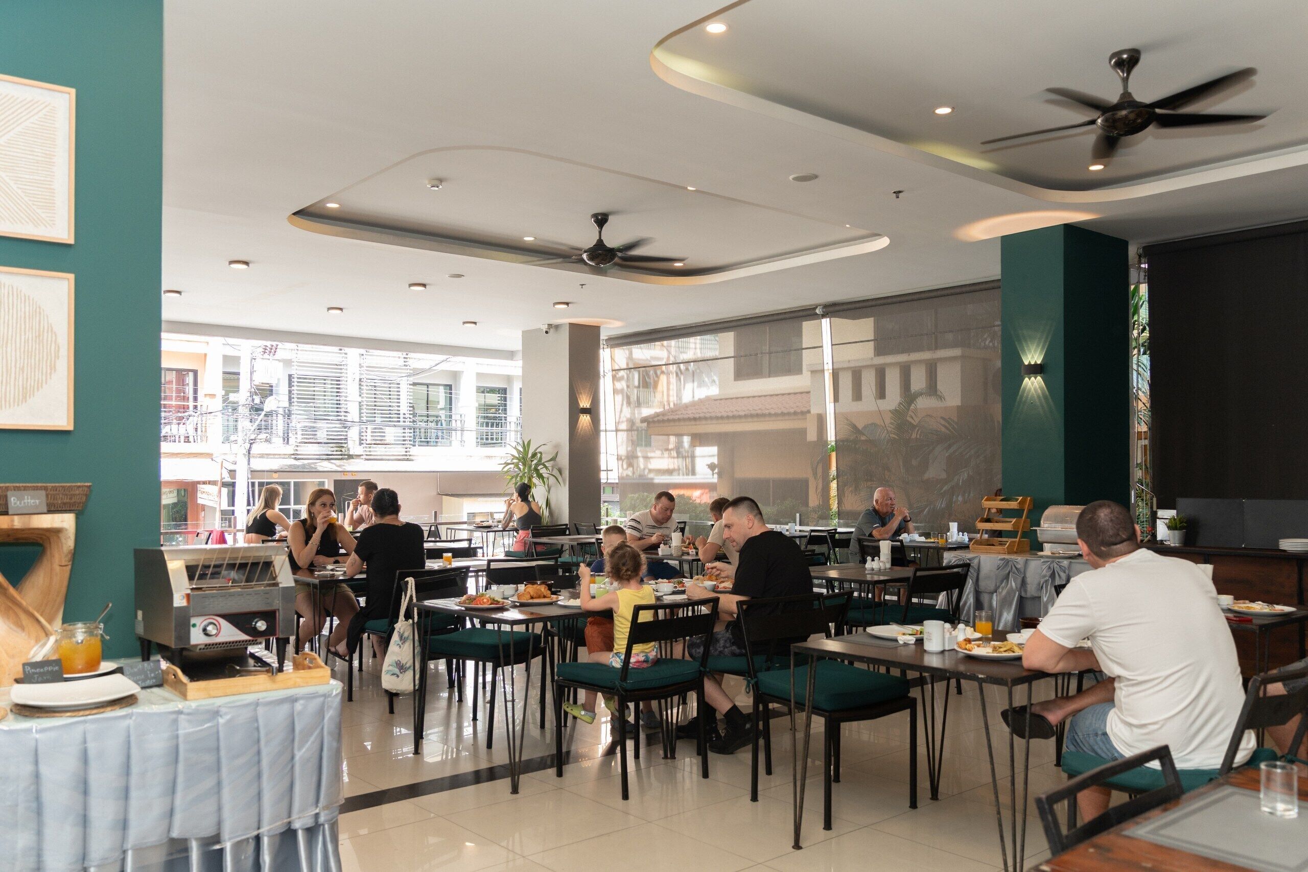 Un vaste espace dédié à la salle à manger, avec de nombreuses tables et chaises, des ventilateurs de plafond et une vue sur l’extérieur grâce à de grandes fenêtres.
