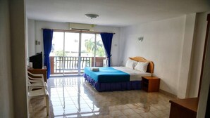 A hotel room with a bed, a desk, a chair, a balcony with curtains, and a view of greenery outside. - Joy Residence (Pattaya)