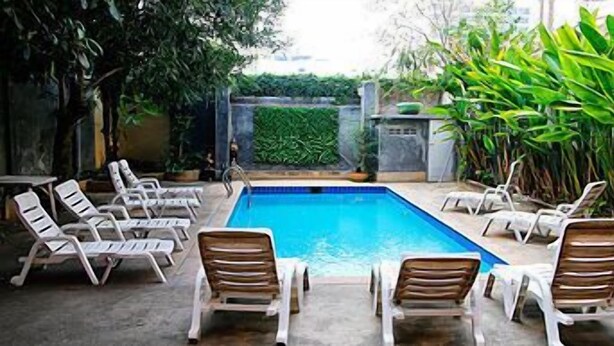 A swimming pool with lounge chairs arranged around it, surrounded by greenery. - Joy Residence (Pattaya)