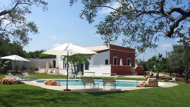 A modern house with a swimming pool, surrounded by a well-maintained lawn and trees.