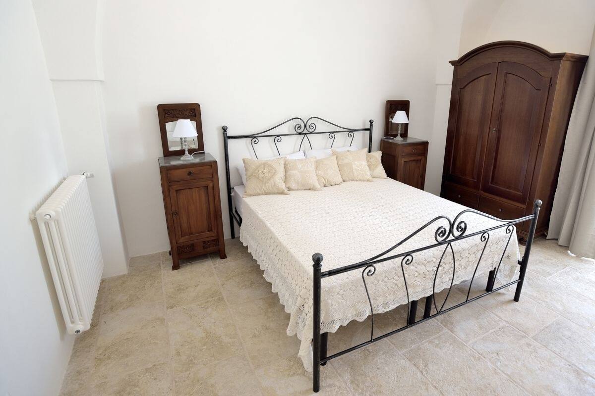 Une chambre à coucher avec un lit en métal, une armoire en bois, une table de chevet avec une lampe et un radiateur.