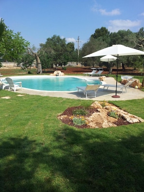 Un patio trasero con piscina, sillas de descanso y un jardín.