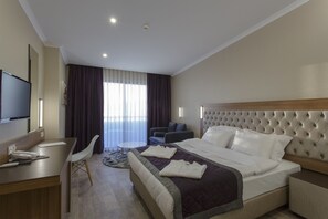Une chambre d’hôtel avec un lit, un bureau, une chaise, une télévision et une fenêtre avec des rideaux.