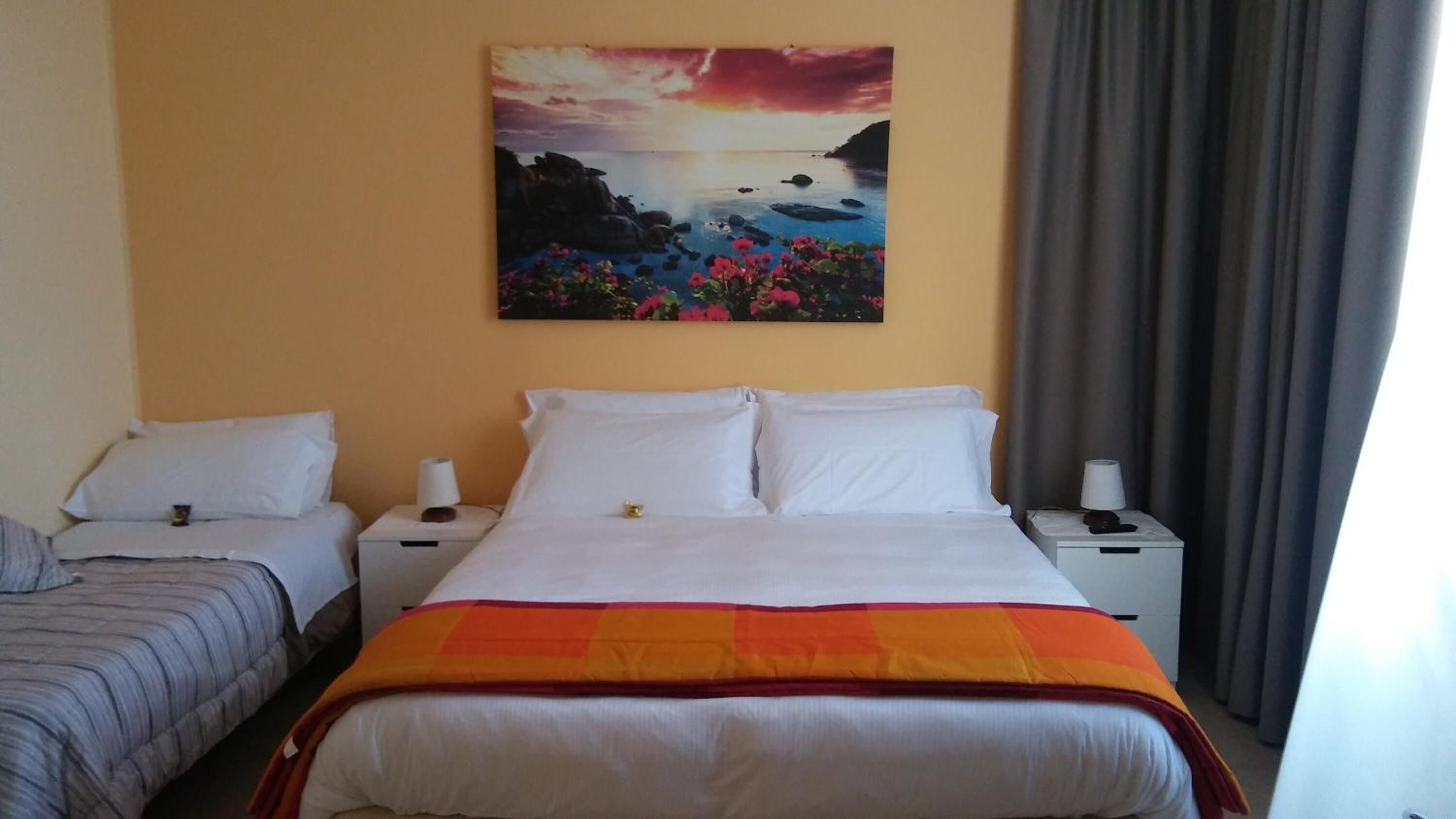 A hotel room with two beds, a painting of a sunset over water, and a view of the sea through the window.