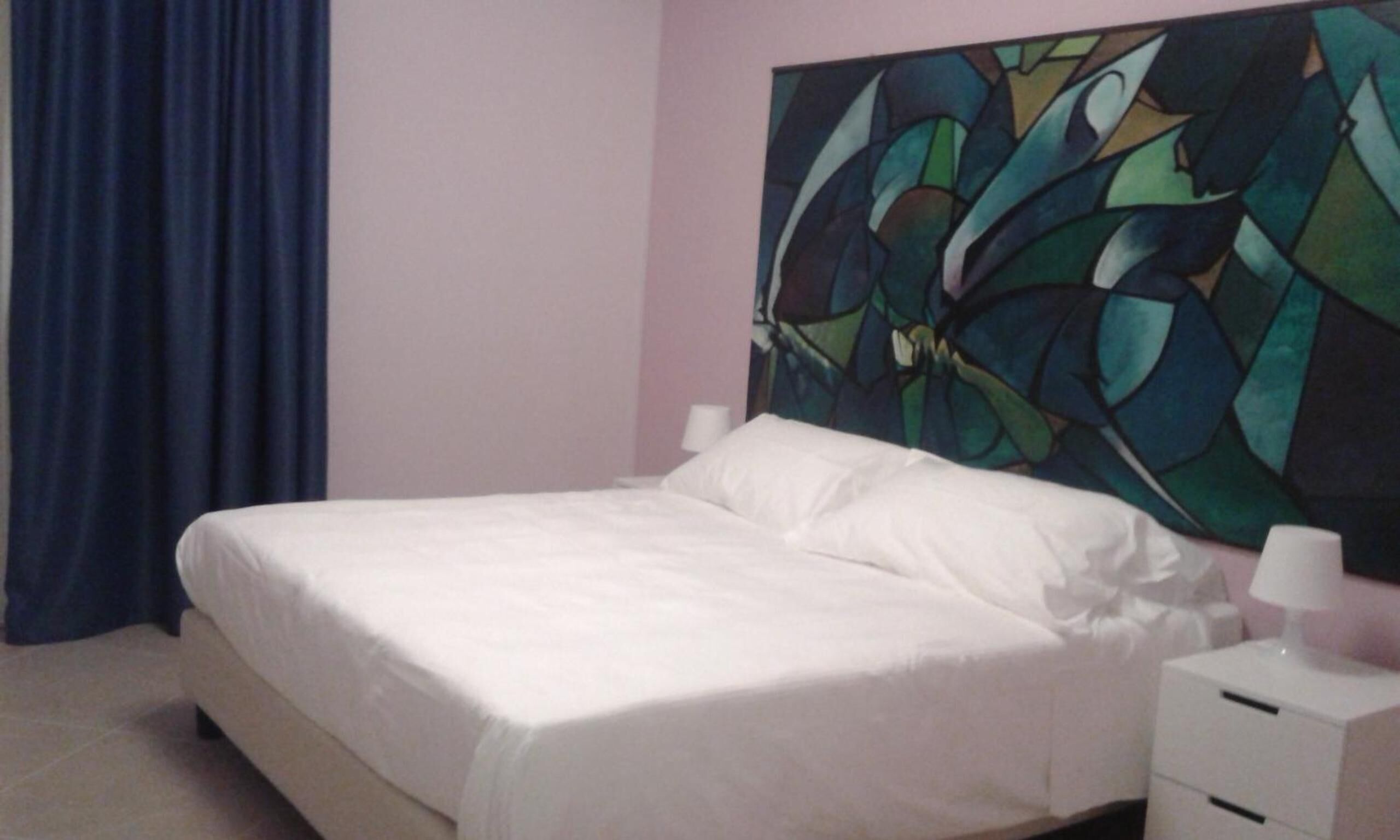 Une chambre à coucher avec un lit, une table de chevet et un grand tableau abstrait accroché au mur.