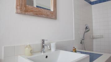 Un baño con lavamanos blanco, espejo, ducha y paredes con azulejos azules.