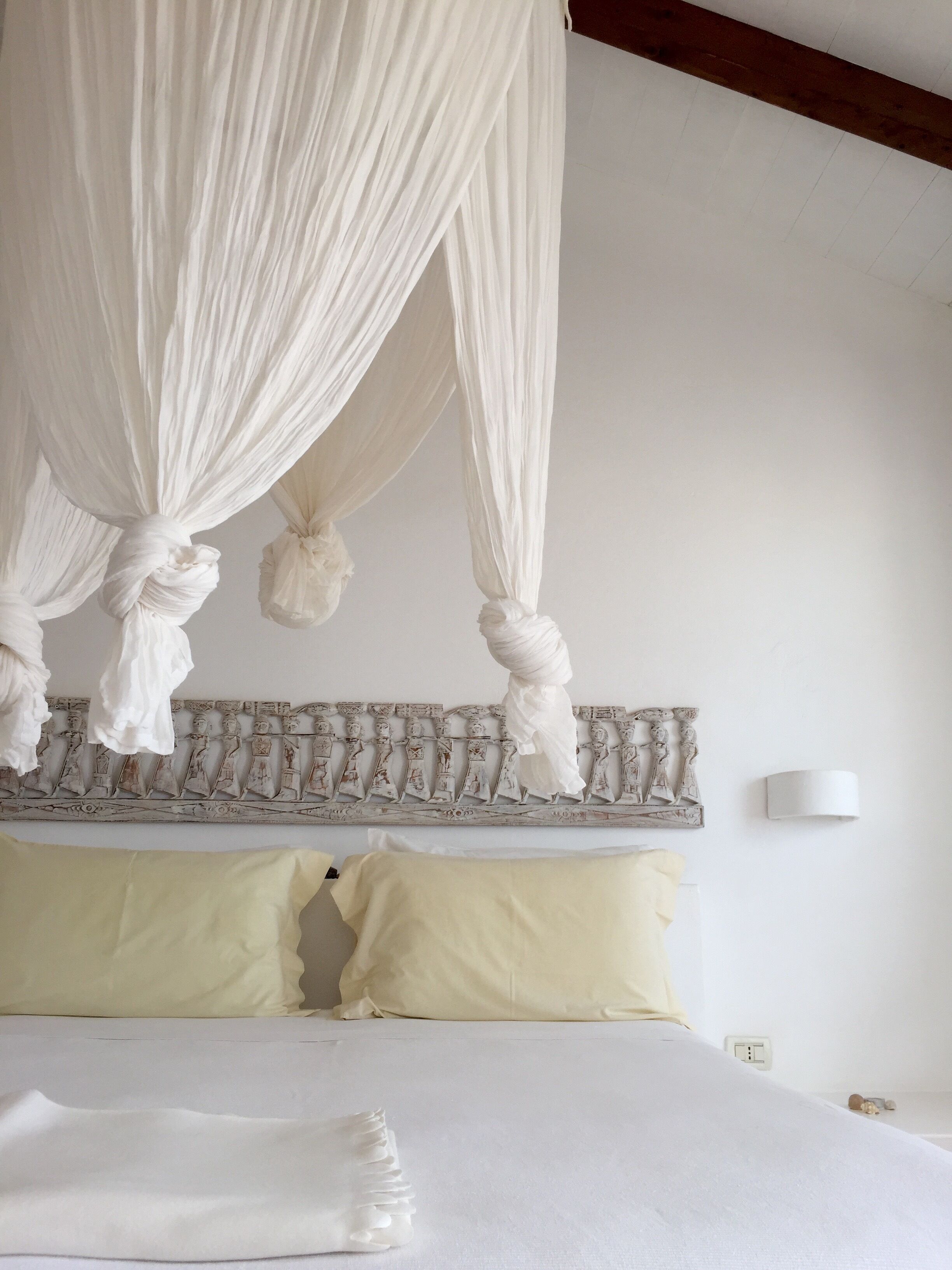Una cama con ropa blanca, un cabecero con figuras talladas y un dosel blanco.