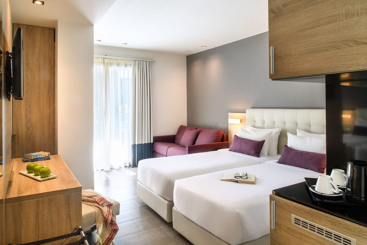 Een hotelkamer met twee bedden, een bureau, een flatscreen televisie, een koffiezetapparaat en een raam met gordijnen.