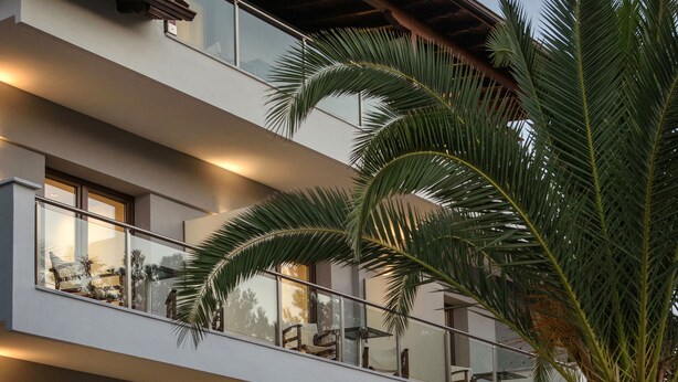 Um hotel com vários andares, varandas, janelas amplas e uma palmeira.