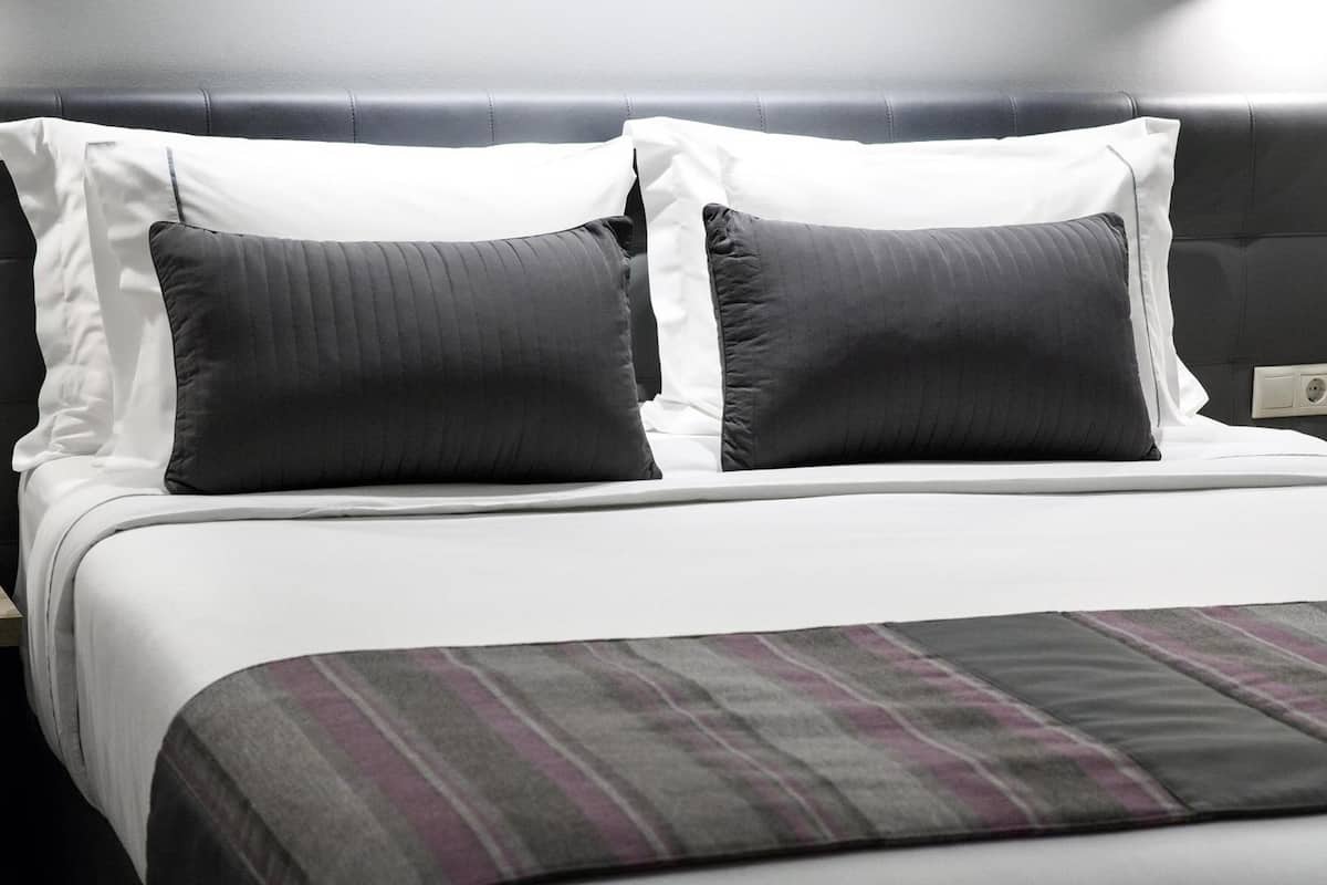 Een keurig opgemaakt bed met witte lakens en twee donkergrijze kussens.